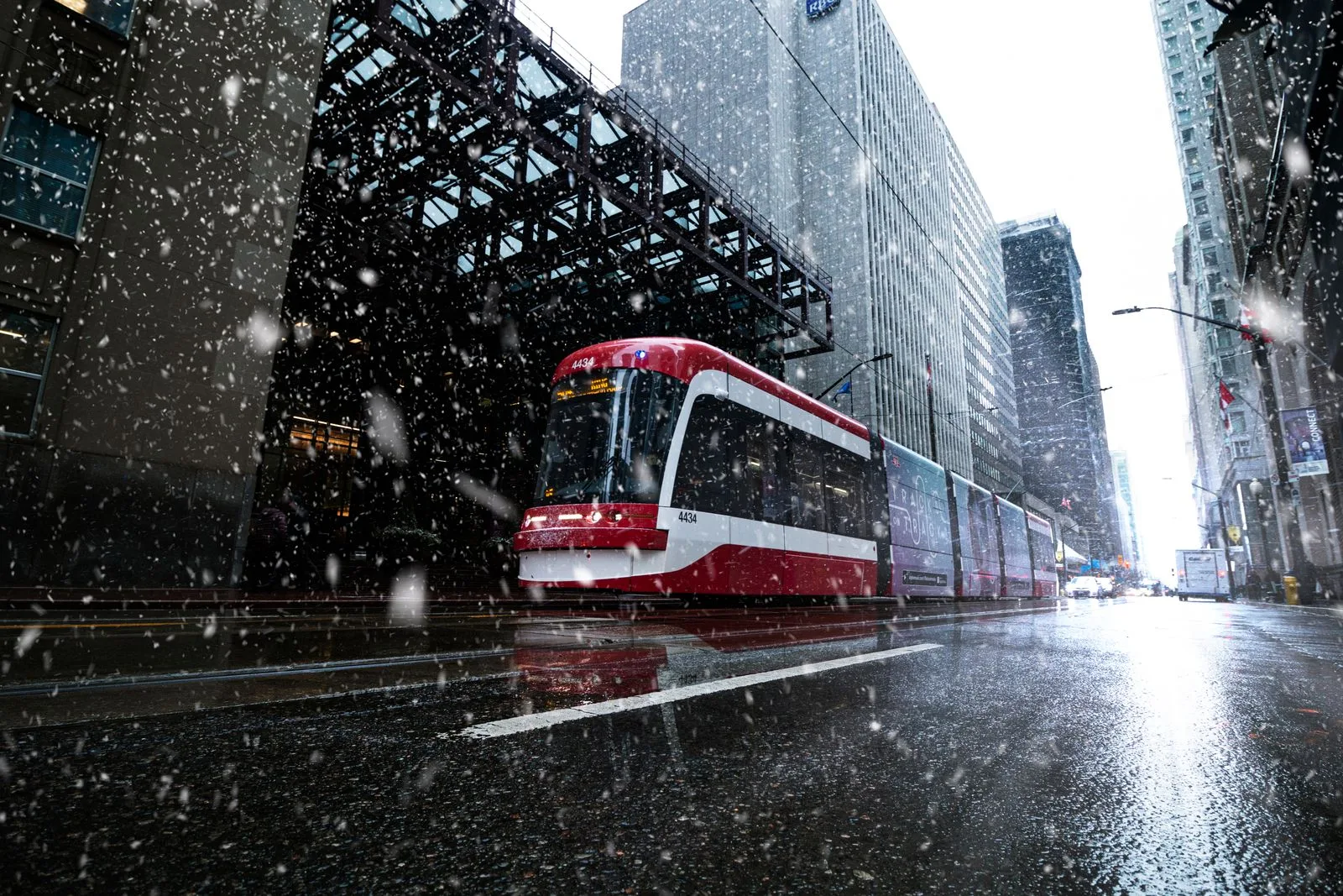 A red TTC streetcar travelling through downtown Toronto during snowfall
